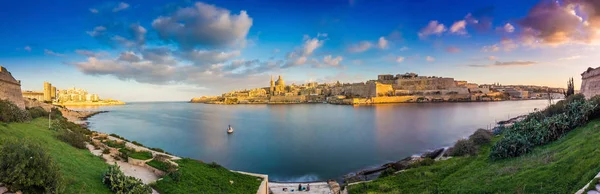 Valletta, Malta - Vista panorâmica da antiga cidade de Valletta e Sliema ao nascer do sol tirada da ilha de Manoel na primavera com barco à vela, céu azul, belas nuvens e grama verde — Fotografia de Stock