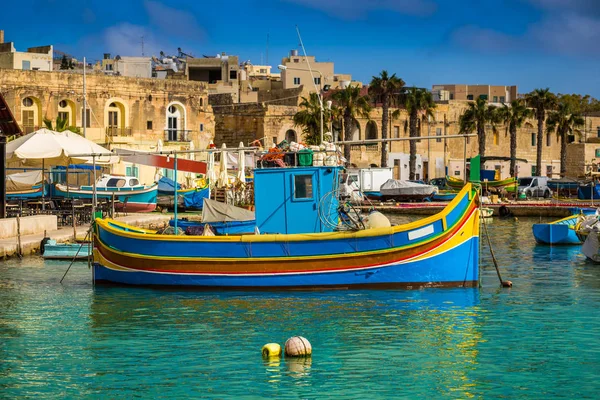 Marsaxlokk, Malta - traditionele kleurrijke maltese Luzzu drijvers in het oude dorp van Marsaxlokk met turquoise zee water en palm bomen op een zomerdag — Stockfoto