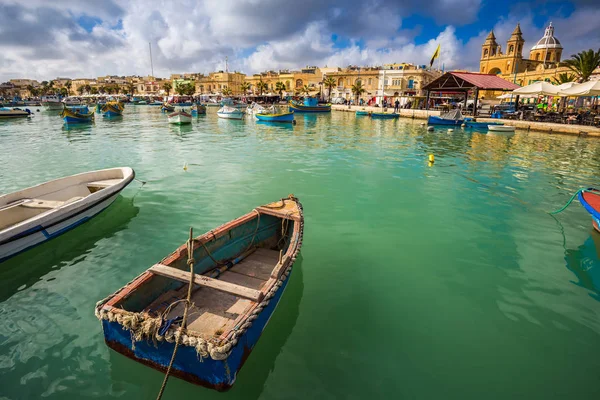 Marsaxlokk, Malta - Los tradicionales y coloridos barcos de pesca malteses de Luzzu en el antiguo mercado de Marsaxlokk con agua de mar verde, cielo azul y palmeras en un día de verano — Foto de Stock