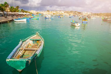 MARSAXLOKK, Malta - geleneksel renkli Malta Luzzu fisherboats eski piyasada Marsaxlokk yeşil deniz su, mavi gökyüzü ve palmiye ağaçlarıyla bir yaz gününde