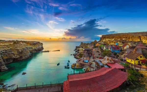 Mellieha, Malta - Skyline view of the beautiful Popeye Village at Anchor Bay at sunset with amazing colorful clouds and sky — Stock Photo, Image