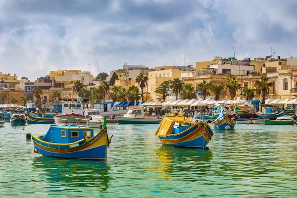 Marsaxlokk, Malta - традиционные цветные мальтийские рыбацкие лодки Luzzu в старой деревне Marsaxlokk с бирюзовой морской водой и пальмами в летний день — стоковое фото