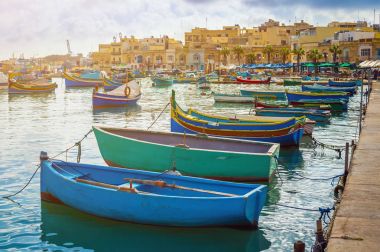 MARSAXLOKK, Malta - geleneksel renkli Malta Luzzu fisherboats eski Marsaxlokk Köyü turkuaz deniz su ve palmiye ağaçlarıyla bir yaz gününde