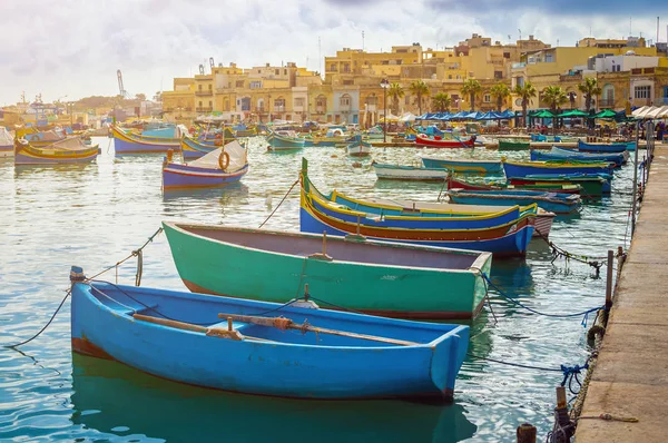 Marsaxlokk, Malta - традиционные цветные мальтийские рыбацкие лодки Luzzu в старой деревне Marsaxlokk с бирюзовой морской водой и пальмами в летний день — стоковое фото