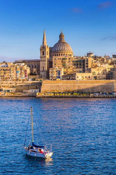 Valletta, Malta - St.Paul 's Cathedral i gyllene timmen på Maltas huvudstad Valletta med segelbåt och vacker blå himmel — Stockfoto