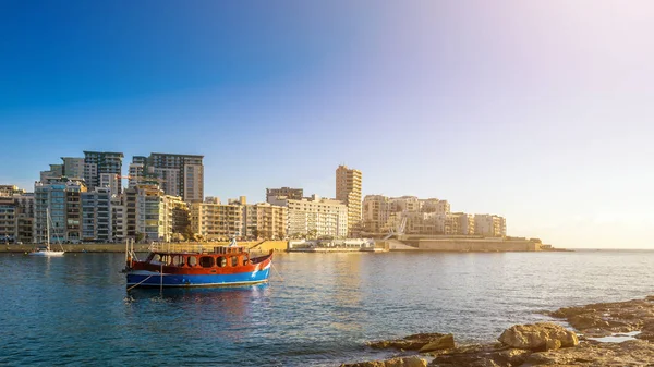 Sliema, Malta - Salida del sol con barco tradicional maltés y apartamentos de Tigne punto tomado de la isla de Manoel en un día caluroso de verano — Foto de Stock