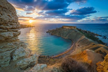 Mgarr, Malta - Panorama of Gnejna bay, the most beautiful beach in Malta at sunset with beautiful colorful sky and golden rocks taken from Ta Lippija clipart