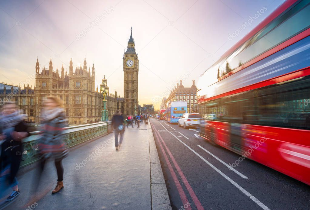 London, England - The iconic Big Ben and the Houses of Parliament with famous red double-decker bus and tourists on the move on Westminster bridge at sunset