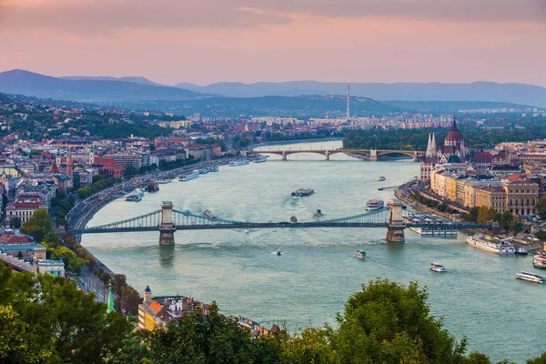 Budapest, Magyarország - panorámás skyline view a naplemente, a híres Széchenyi Lánchíd, Margit híd, Margit-sziget és Magyarország Parlament, a Budai hegyek a háttérben színes égbolt — Stock Fotó