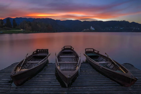 Bled, Slovenië - traditionele boten bij Lake Bled met prachtige dramatische zonsondergang en de veronderstelling van Mary bedevaartskerk en bergen op de achtergrond bij zonsondergang — Stockfoto