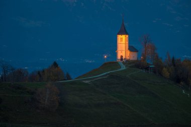 Jamnik, Slovenya - Jamnik mavi saatte ışıklı St. Primoz kilise ile. Julian Alps, arka plan