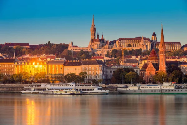 Budapeste, Hungria - Hora de ouro pela manhã ao lado de Buda com o Castelo de Buda, a igreja de St. Matthias e o Bastião dos Pescadores com navios antigos no rio Danúbio e céu azul claro — Fotografia de Stock