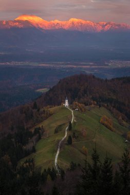 Jamnik, Slovenya - güzel altın günbatımı hava görünümünü Jamnik St. Primoz Kilisesi. Julian Alps, arka planda güneş ışığı