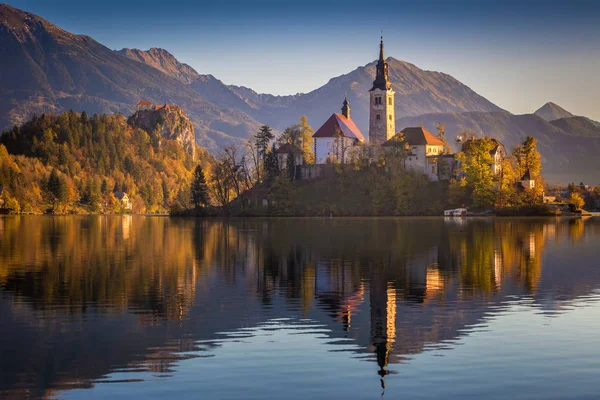 Блед, Словения - осенний восход солнца на озере Блед со знаменитой паломнической церковью Успения Марии с замком Блед и Юлианскими Альпами на заднем плане — стоковое фото