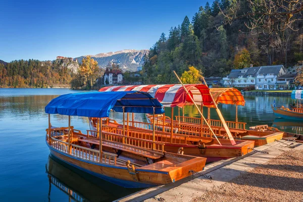 Bled, Slovenia - Tradizionali barche rosse, arancioni e blu Pletna sotto il sole autunnale sul lago di Bled con il castello di Bled sullo sfondo — Foto Stock