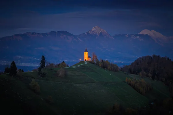 Jamnik, Eslovenia - Hora azul en Jamnik con la iglesia iluminada de St. Primoz. Julián Alpes en el fondo —  Fotos de Stock