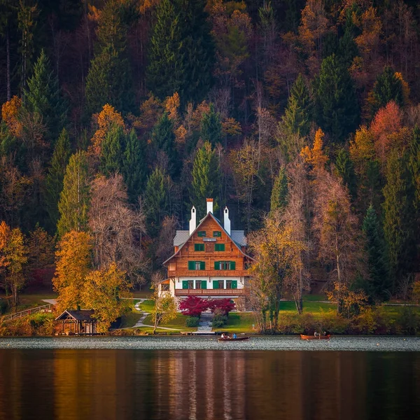 Bled, Słowenia - typowe słoweńskie alpen dom jeziorem Bled z łodzi i piękne kolorowe jesień las na zachód słońca — Zdjęcie stockowe