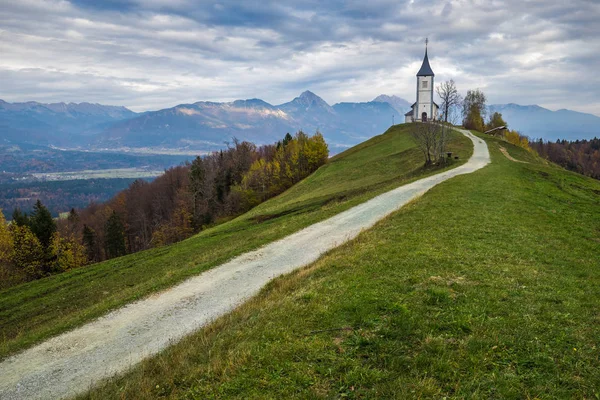 Jamnik, Eslovenia - La hermosa iglesia de San Primoz en Eslovenia cerca de Jamnik con hermosas nubes y los Alpes Julianos en el fondo —  Fotos de Stock