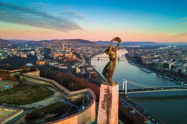 布达佩斯, 匈牙利-自由女神像与布达城堡皇宫和链桥背景的空中地平线观。清晨的日出与蓝天白云 — 图库照片
