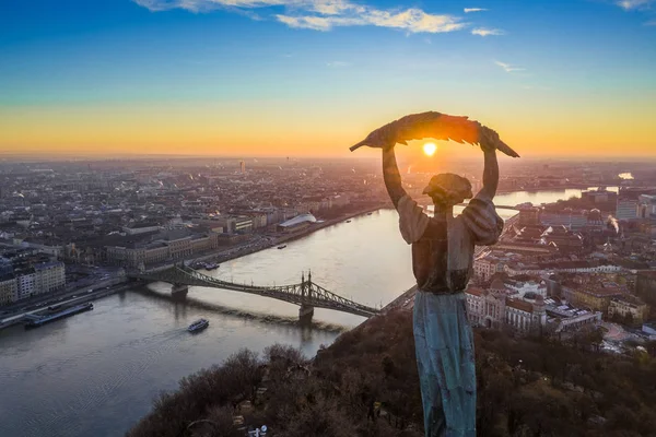 Budapest, Hungary - Aerial panoramic sunrise view at the Statue of Liberty with Liberty Bridge and sightseeing boat on River Danube taken from Gellert Hill