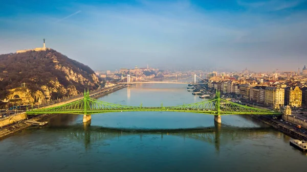 Budapest, Hungary - Aerial skyline view of beautiful Liberty Bridge (Szabadsag Hid) on a sunny morning with Gellert Hill, Citadella, Statue of Liberty, Elisabeth Bridge and Buda Castle Royal Palace at background with clear blue sky