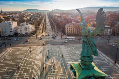 Budapest, Hungary - Angel sculpture from behind on the top of Heroes' Square at sunset with Andrassy street and the skyline of Budapest at background clipart