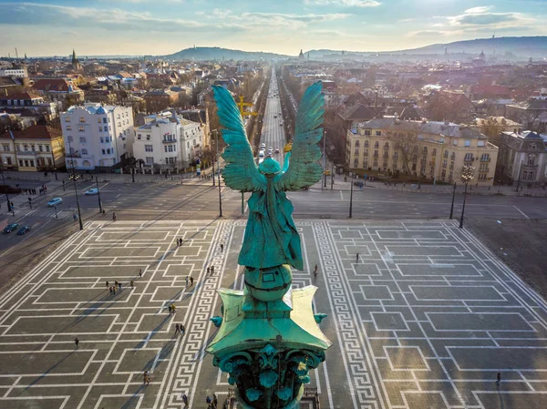 Budapest, Hungary - Angel sculpture from behind on the top of Heroes' Square at sunset with Andrassy street and the skyline of Budapest at background — Stock Photo, Image