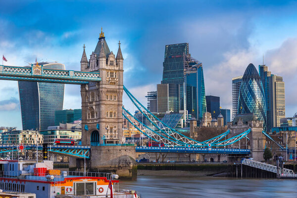London, England - The famous Tower Bridge with iconic red double-decker buses on it and skyscrapers of Bank District at background