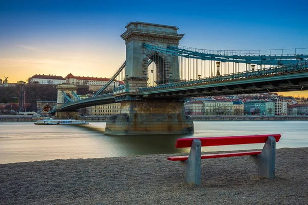 Budapešť, Maďarsko - slavný Széchenyi Řetězový most s tradičním červeném lavičce a vyhlídková loď na řece Dunaji při západu slunce. Jasně modré obloze — Stock fotografie