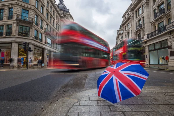 London, Anglia - brit esernyő elfoglalt Regent Street, ikonikus piros emeletes buszok a mozgásban — Stock Fotó