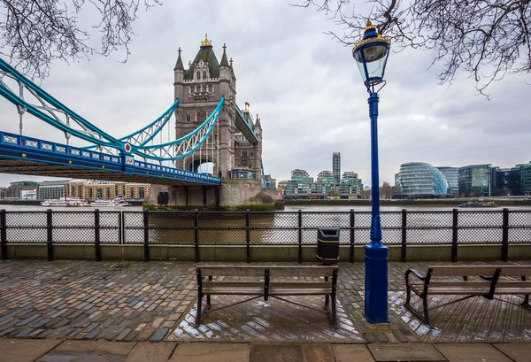 Londres, Inglaterra - Iconic Tower Bridge com bancada e luz de rua em um dia nublado com escritórios no fundo — Fotografia de Stock