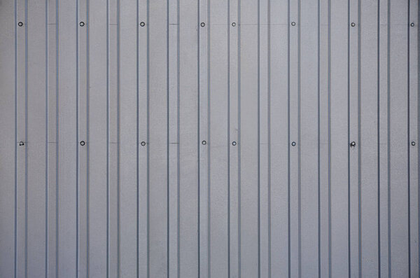 Siding, metal panels texture closeup in the daytime outdoors. Metal wall or fence embossed metal sheets. Terrain and large metal sheet as a barrier or fence