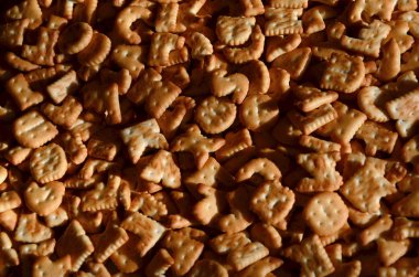 Bir sürü küçük sarı tuzlu kraker bir Ahşap Doğrama Kurulu yakın çekim yalan yazdırılan İngilizce harf şeklinde. Arka plan görüntüsü Tuzlu bisküvi