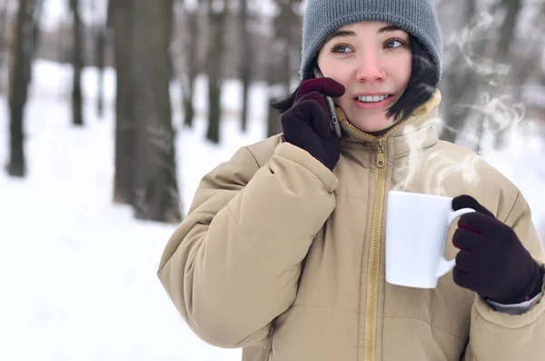Retrato de invierno de niña con teléfono inteligente y taza de café — Foto de Stock