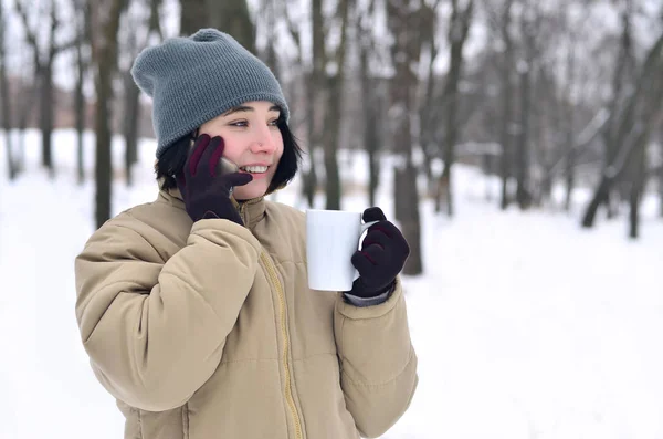 Зимовий портрет молодої дівчини зі смартфоном і чашкою кави — стокове фото