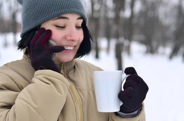 Зимовий портрет молодої дівчини зі смартфоном і чашкою кави — стокове фото