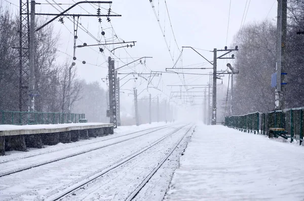 Railway landscape in the cold winter season. Snow-covered railway station platform and foggy overcast sky during a heavy snowfall