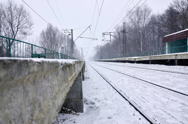 Railway landscape in the cold winter season. Snow-covered railway station platform and foggy overcast sky during a heavy snowfall