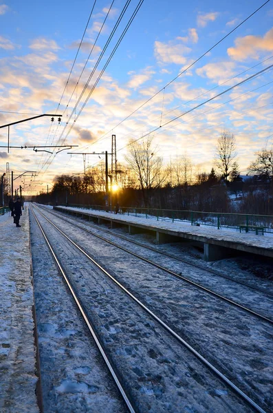 Evening winter landscape with the railway station. Snow-covered railway platform under the sun light at sunset. A place where people waiting for a train