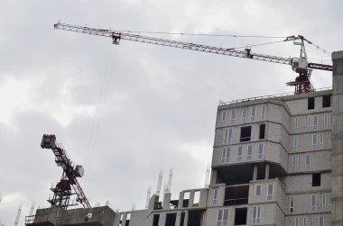 Yüksek binaların yapım aşamasında karşı açık mavi gökyüzü ile yer içinde çalışan uzun boylu vinç. Vinç ve çalışma ilerleme boşaltmak ile bina