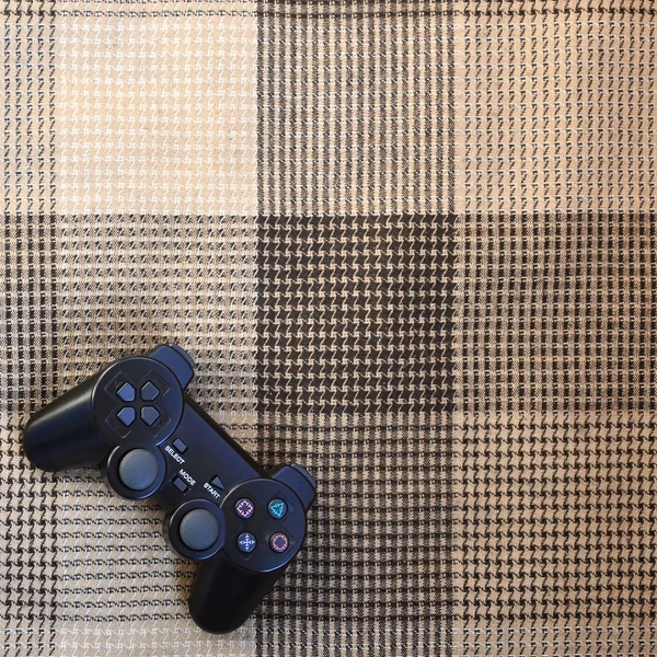 モダンな黒のビデオゲームのコント ローラーは 市松模様のベージュと黒のベールまたは格子縞にあります 子供のゲーム エンターテイメント レクリエーションの概念としてプラスチック製ジョイスティック — ストック写真