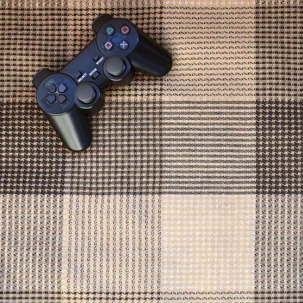 The video game controller from the game console is on the checkered sofa. Wireless device for controlling during video games