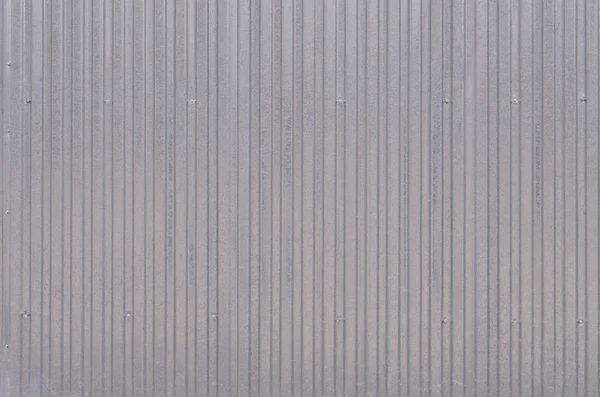 Siding, metal panels texture closeup in the daytime outdoors. Metal wall or fence embossed metal sheets. Terrain and large metal sheet as a barrier or fence