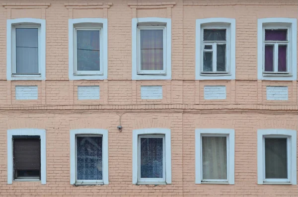 The texture of a brick wall with a few windows. Glazed windows in the wall of an old bricks in daylight outdoors