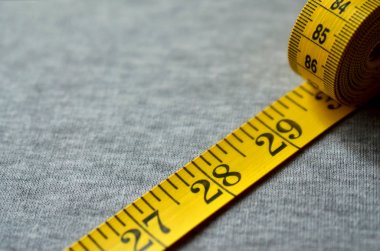 Sarı ölçüm bandı üzerinde gri bir örme kumaş yatıyor