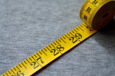 Sarı ölçüm bandı üzerinde gri bir örme kumaş yatıyor