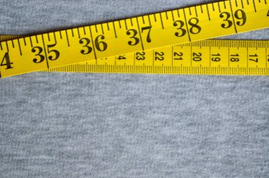 Sarı ölçüm bandı üzerinde gri bir örme kumaş yatıyor