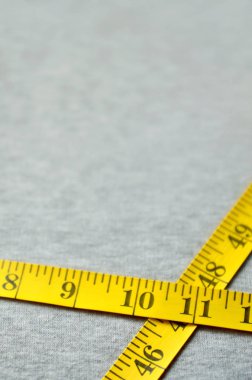 Cm veya inç şeklinde sayısal göstergeler ile sarı renk ölçüm bandı üzerinde gri bir örme kumaş yatıyor. Arka plan görüntüsü dikiş kıyafetler, insanlar için hakkında kim zayıflama