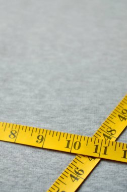 Sarı ölçüm bandı üzerinde gri bir örme kumaş yatıyor