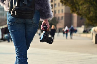 Arkadan görünüş ile modern bir Slr fotoğraf makinesi bulanık bir kalabalık street karşı onun elinde bir kadın fotoğrafçı